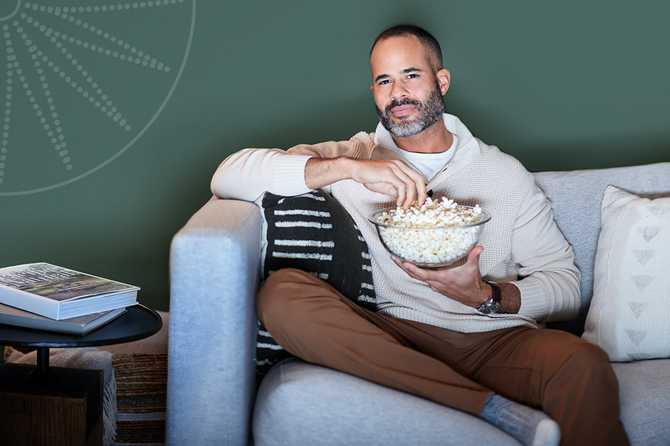 young man sitting on his couch watching TV and eating popcorn